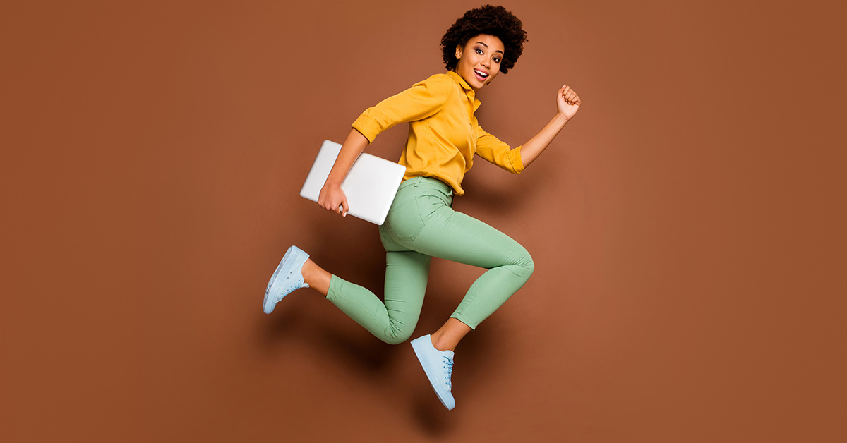 A woman in business casual dress sprints through the air holding a laptop in one hand.