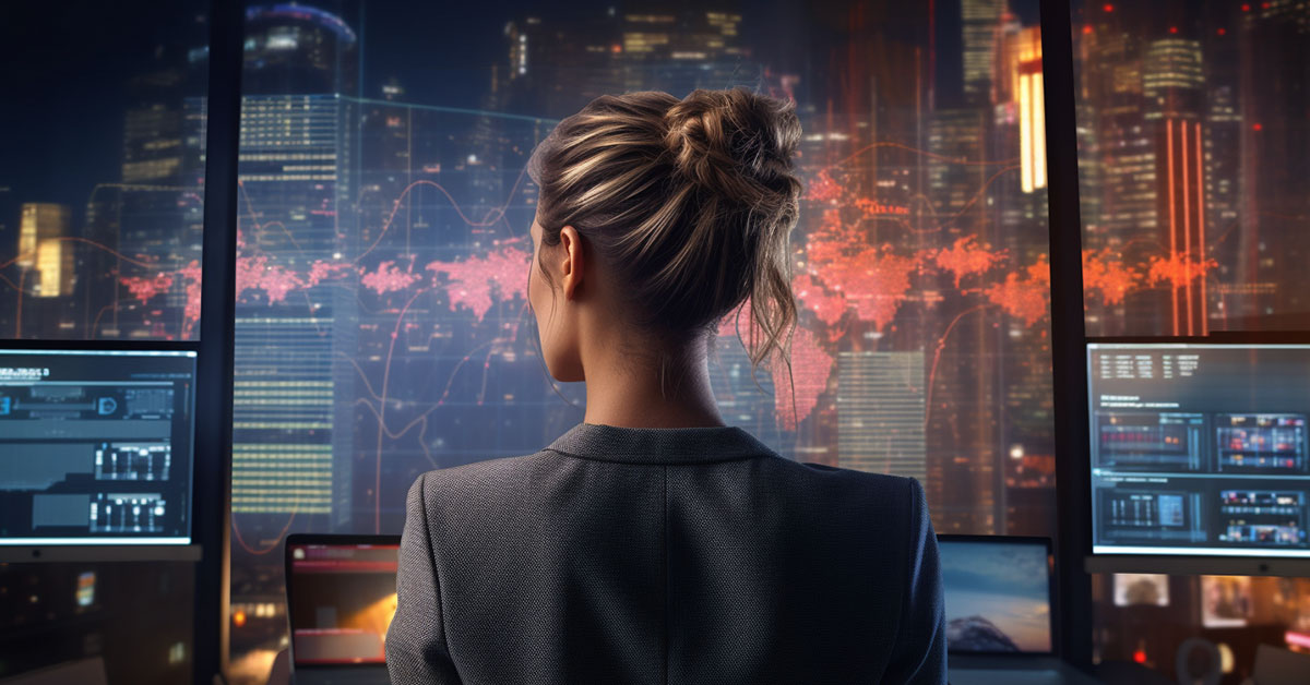 A business woman with a blazer on has her back to the camera. She is looking at a full wall of digital screens full of maps and statistics, representing the data behind the media buying trends of 2024